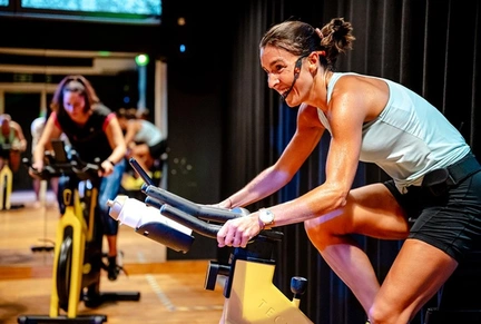 Lesgever doet oefeningen op een spinning fiets in de fitnesszaal van LAGO CLUB Grimbergen en maakt plezier tijdens een groepsles cycling.  