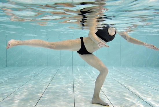 Vrouw toont Zumba oefening tijdens een aquagymles in groep in het zwembad van LAGO CLUB fitness Grimbergen. 