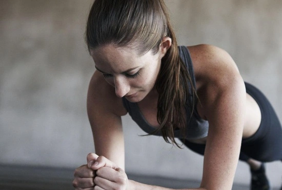 Vrouw doet plankoefening tijdens een groepsles voor versteviging van buik- en rugspieren in LAGO CLUB fitness Grimbergen.