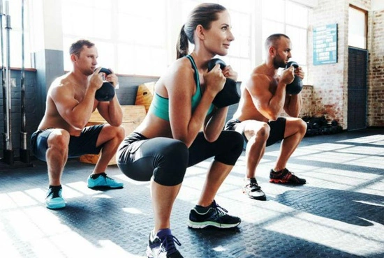 Vrouwen en mannen doen oefeningen met gewichten tijdens een cardio- en krachttraining in groep in LAGO CLUB fitness Grimbergen. 